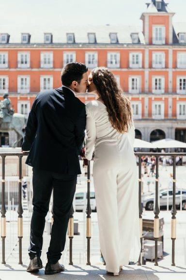 Pareja de espaldas besándose frente a una plaza con edificios coloridos.